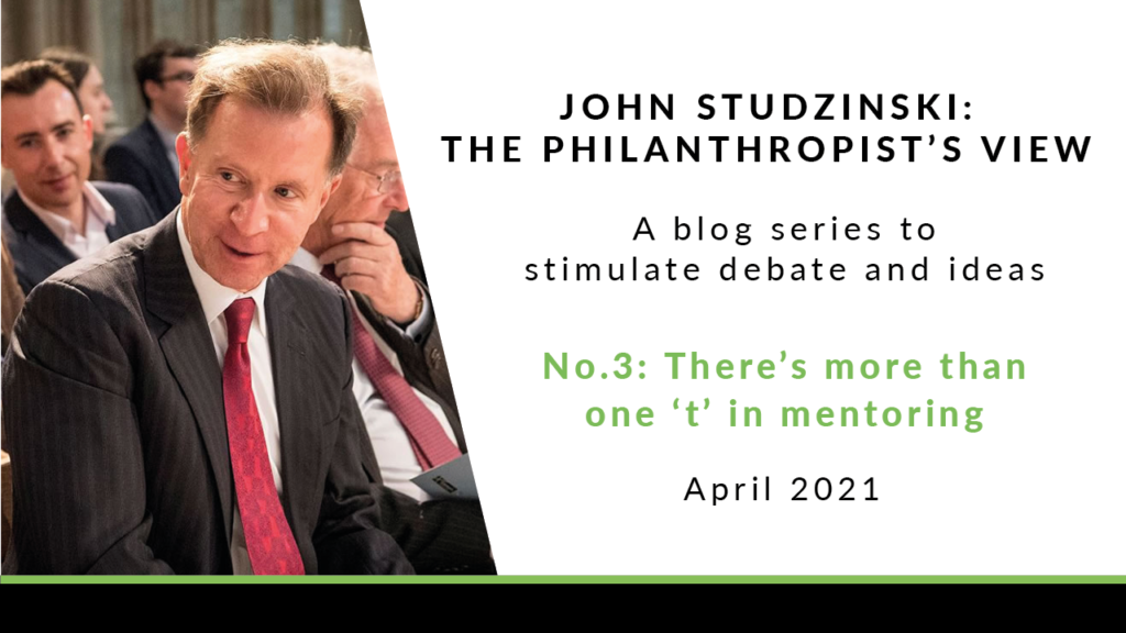 To the left is a photo of John Studzinski, sat in an audience. He is wearing a black jacket, a white shirt and a red tie. He has short grey hair, and is leaning forwards slightly, talking to the person sat next to him. To the right of the image is a white background with black text saying 'John Studzinski - Philanthropist's View. A blog series to stimulate debate and ideas. No. 3: There's more than one 't' in mentoring. April 2021'