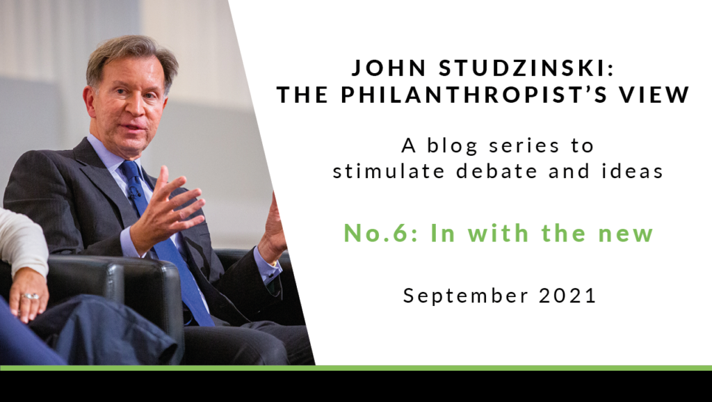 To the left is a photo of John Studzinski, sat on a black leather chair, wearing a black jacket, a light blue shirt, and a dark blue tie. He has short grey hair, and is talking to someone off camera. To the right of the image is a white background with black text saying 'John Studzinski - Philanthropist's View. A blog series to stimulate debate and ideas. No. 6: In with the new. September 2021'.