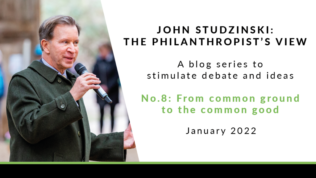 To the left is a photo of John Studzinski, stood outside in a dark green coat, holding a microphone and talking. He has short grey hair, and is looking to the side. To the right of the image is a white background with black text saying 'John Studzinski - Philanthropist's View. A blog series to stimulate debate and ideas. No. 8: From common ground to the common good. January 2022'.