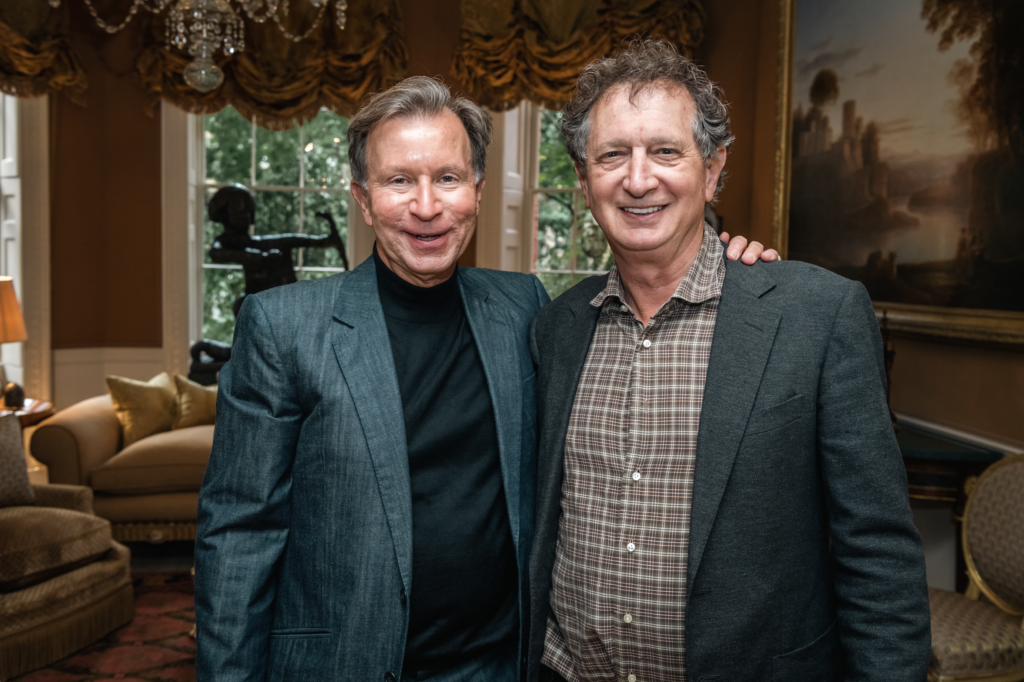 John Studzinksi and David Lan stand side-by-side in a grand living room. John has his arm around David, they are smiling and are dressed in business attire.