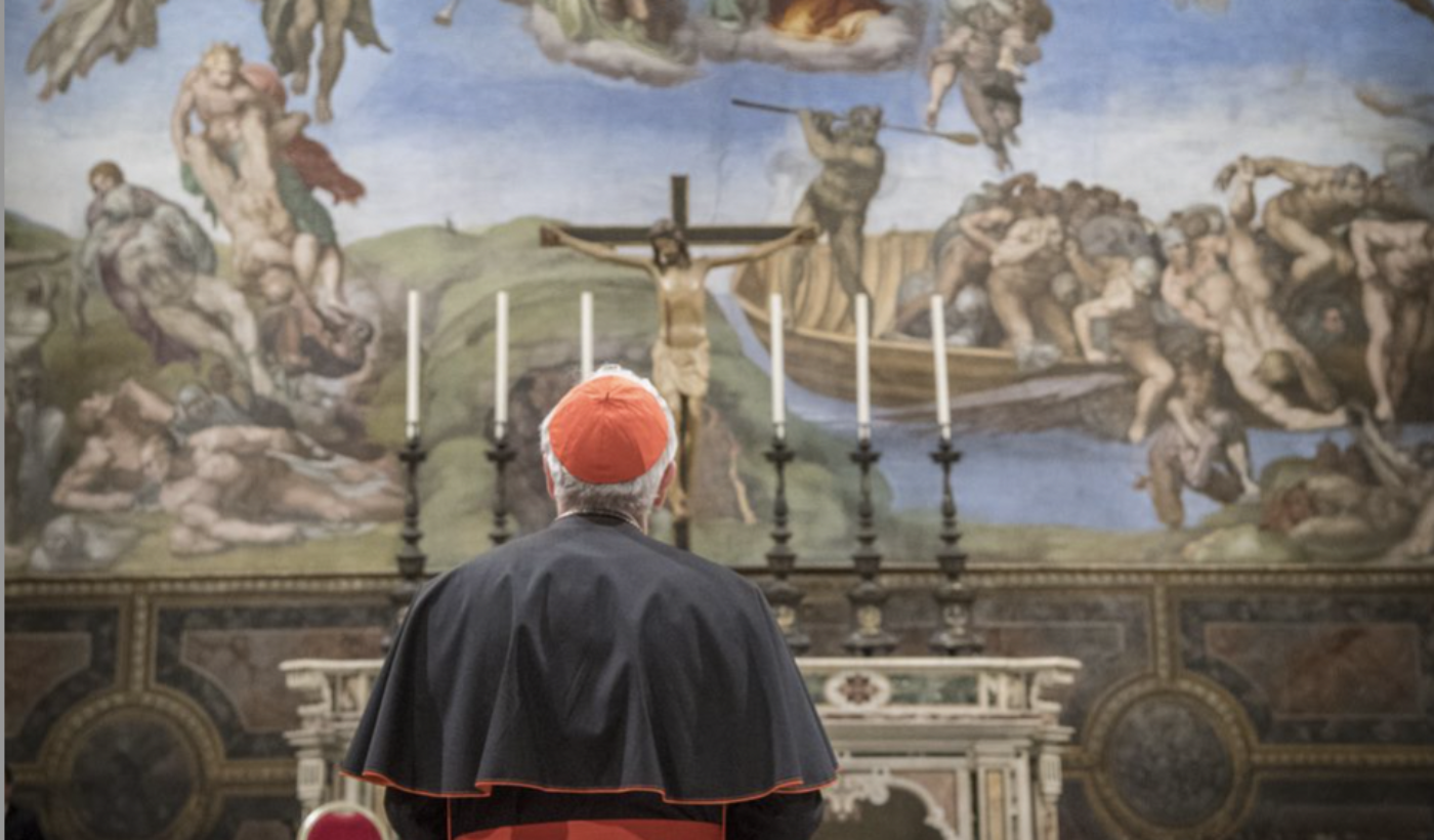 The back of Cardinal Nichols, who is stood inside the Sistine Chapel, looking at a tall wall which is covered completely in a grand painting.