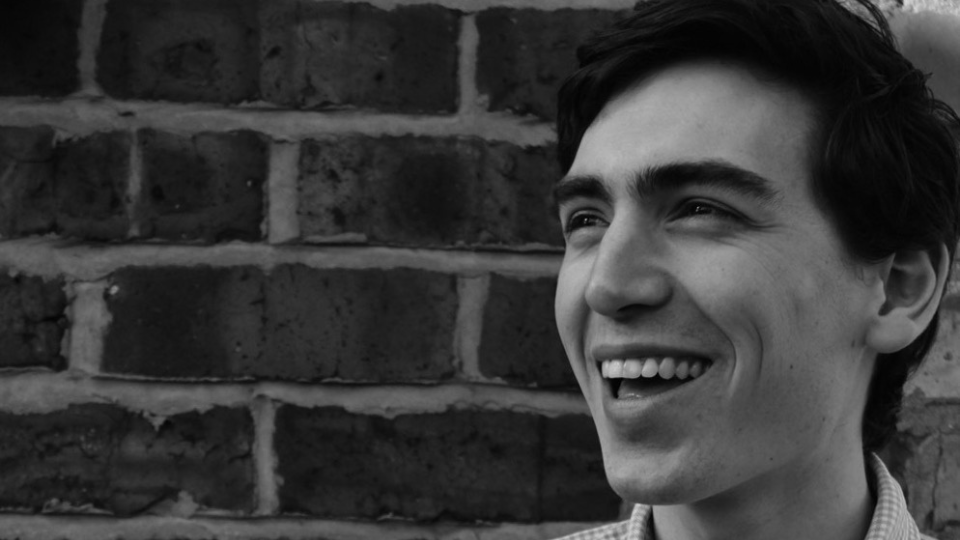 A black and white headshot of Charlie Perry, wearing a checkered shirt, smiling off camera.