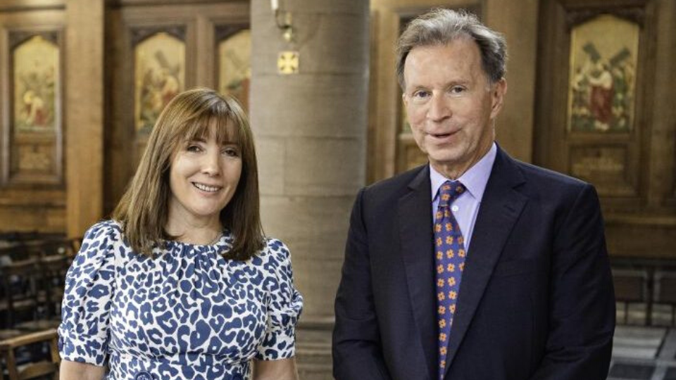 A photo of Managing director Harriet Capaldi and Founder and chairman John Studzinski, standing next to each other inside a grand looking church, dressed in smart attire and smiling at the camera.